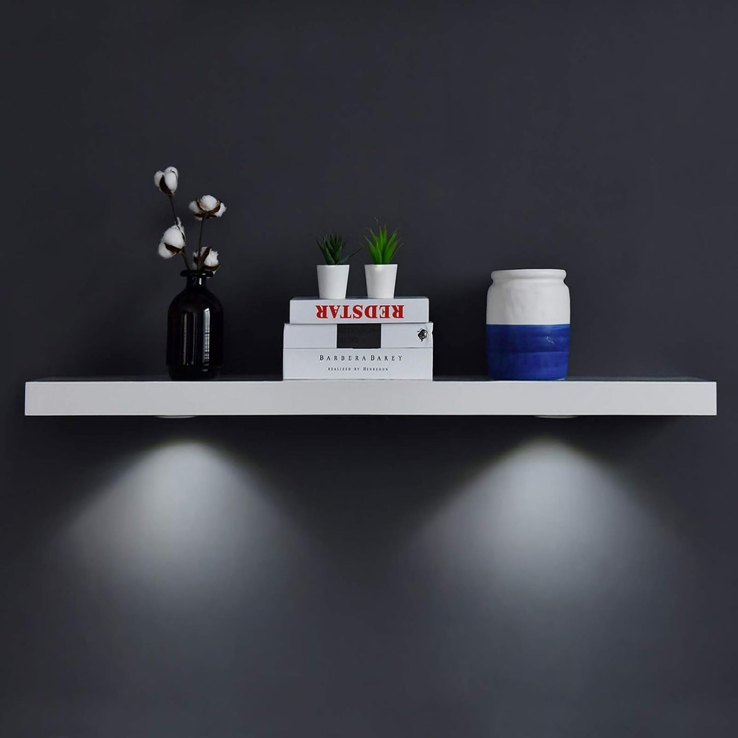 White floating shelf with touch-sensing LED lights displaying books and decor items on a dark wall.